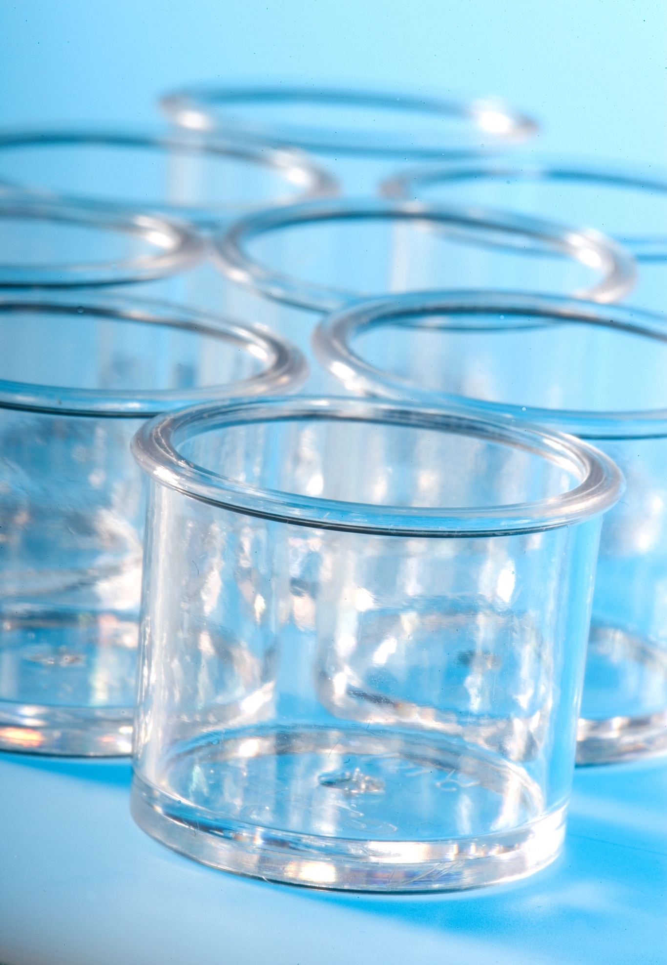 Several clear, empty cylindrical glass jars with thick rims, arranged on a light blue surface.